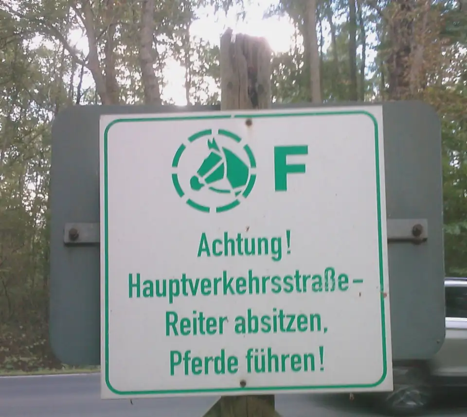 Grünes Schild: Achtung Hauptverkehrsstraße – Reiter absitzen, Pferde führen